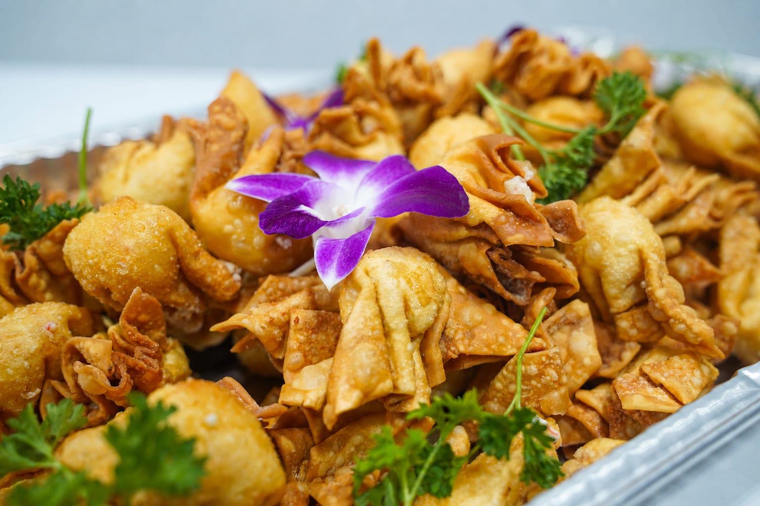A catering tray of golden fried appetizers garnished with parsley and a purple orchid